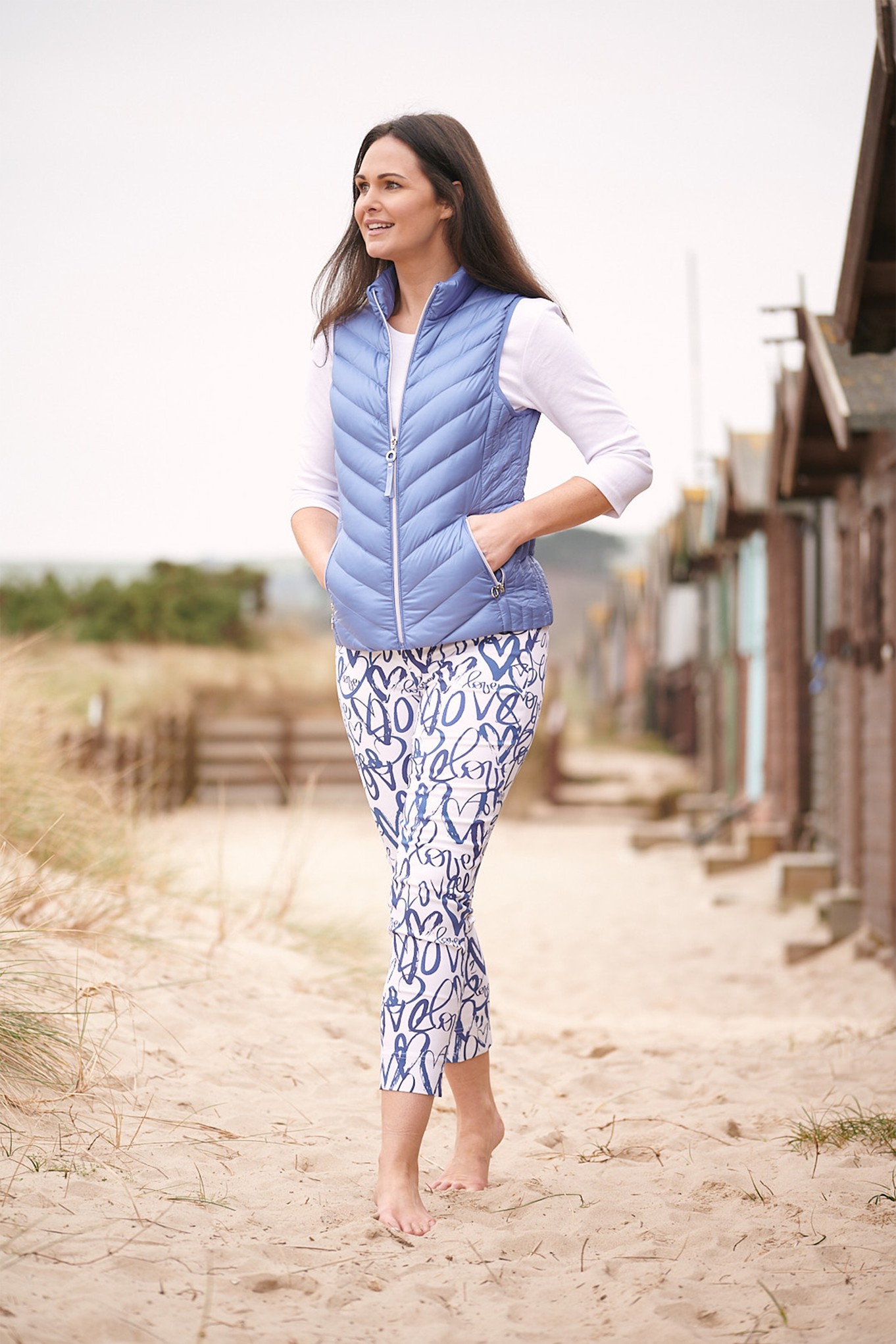 blue and white love print ankle grazer trousers with blue gilet and white top on the beach